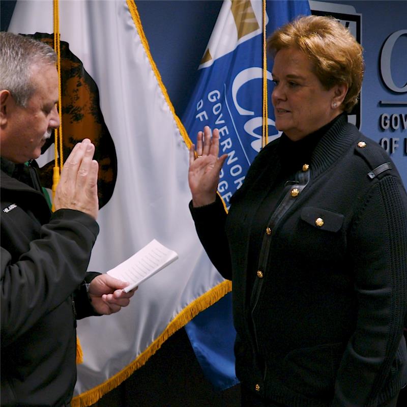 5281674b-307d-4082-9e7b-b9d4104b58d0 Cal OES Director Nancy Ward getting sworn in, with her right hand raised. There are California and Cal OES flags in the background.