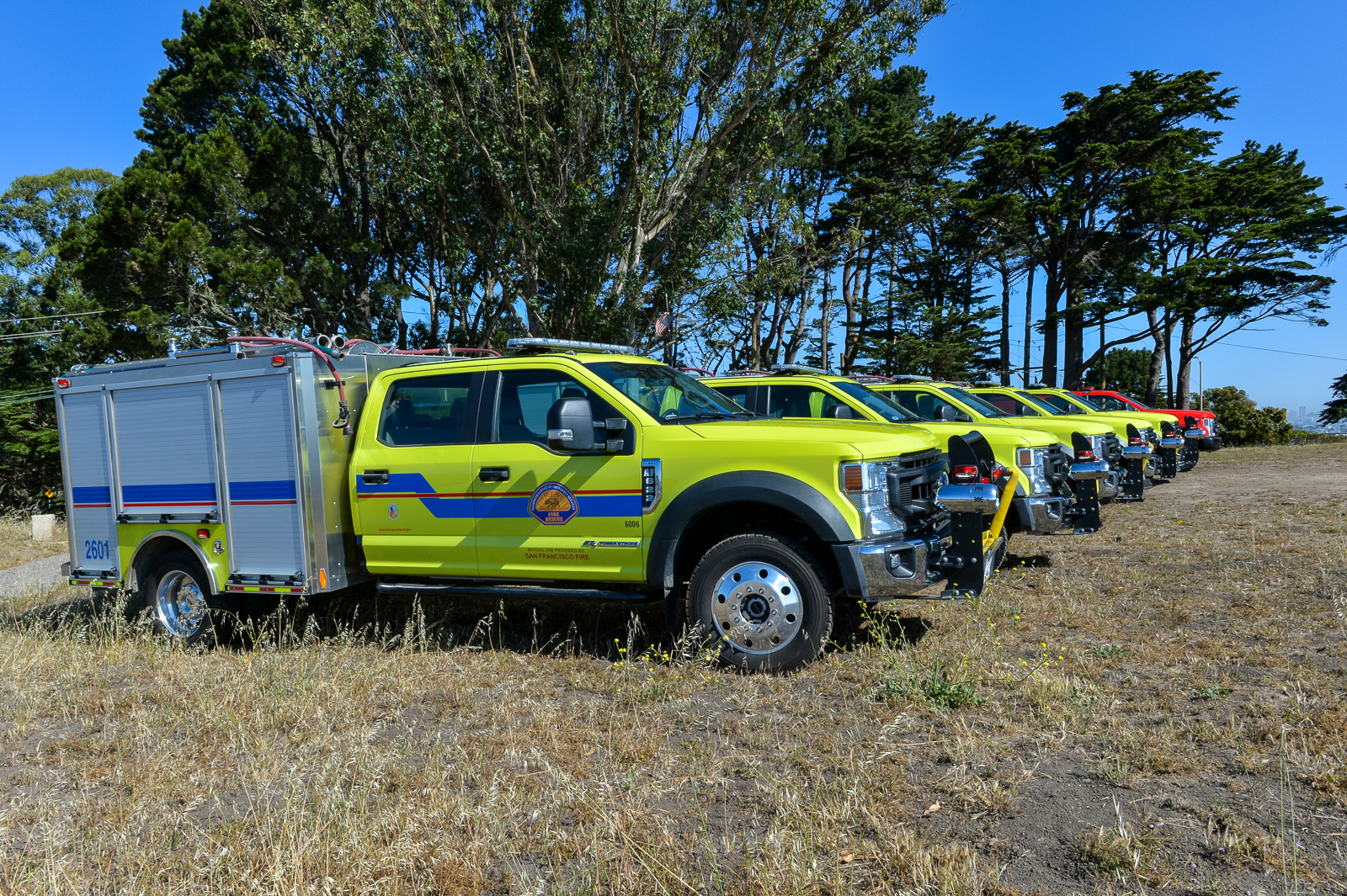 five bright green Cal OES fire engines are lined up in a row. Behind them is a bright red fire engine