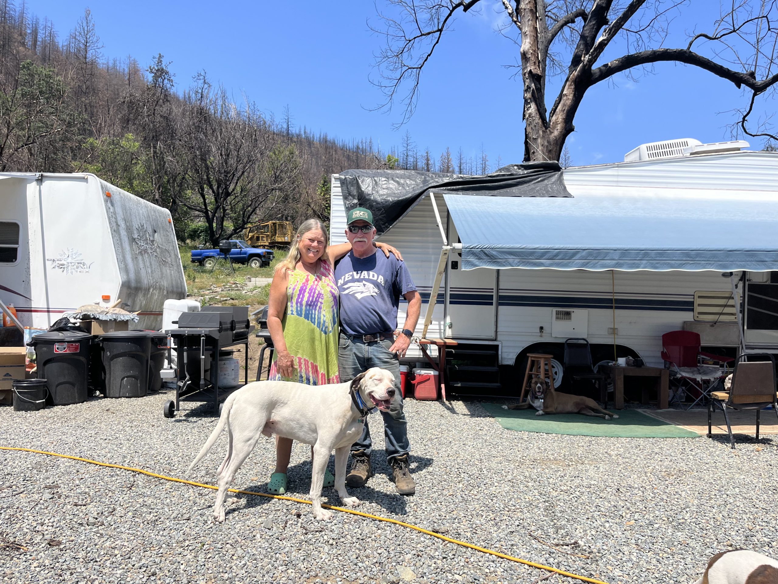 Two people and a big dog stand in front of trailers where debris removal occurred. 