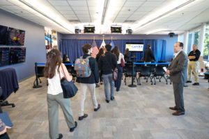 A group of people walk into a room in a row. Two men watch as they walk in.