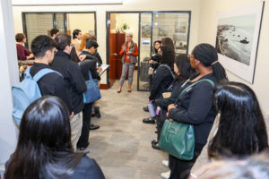 A group of people stand in two rows facing a woman, standing in a doorway speaks.