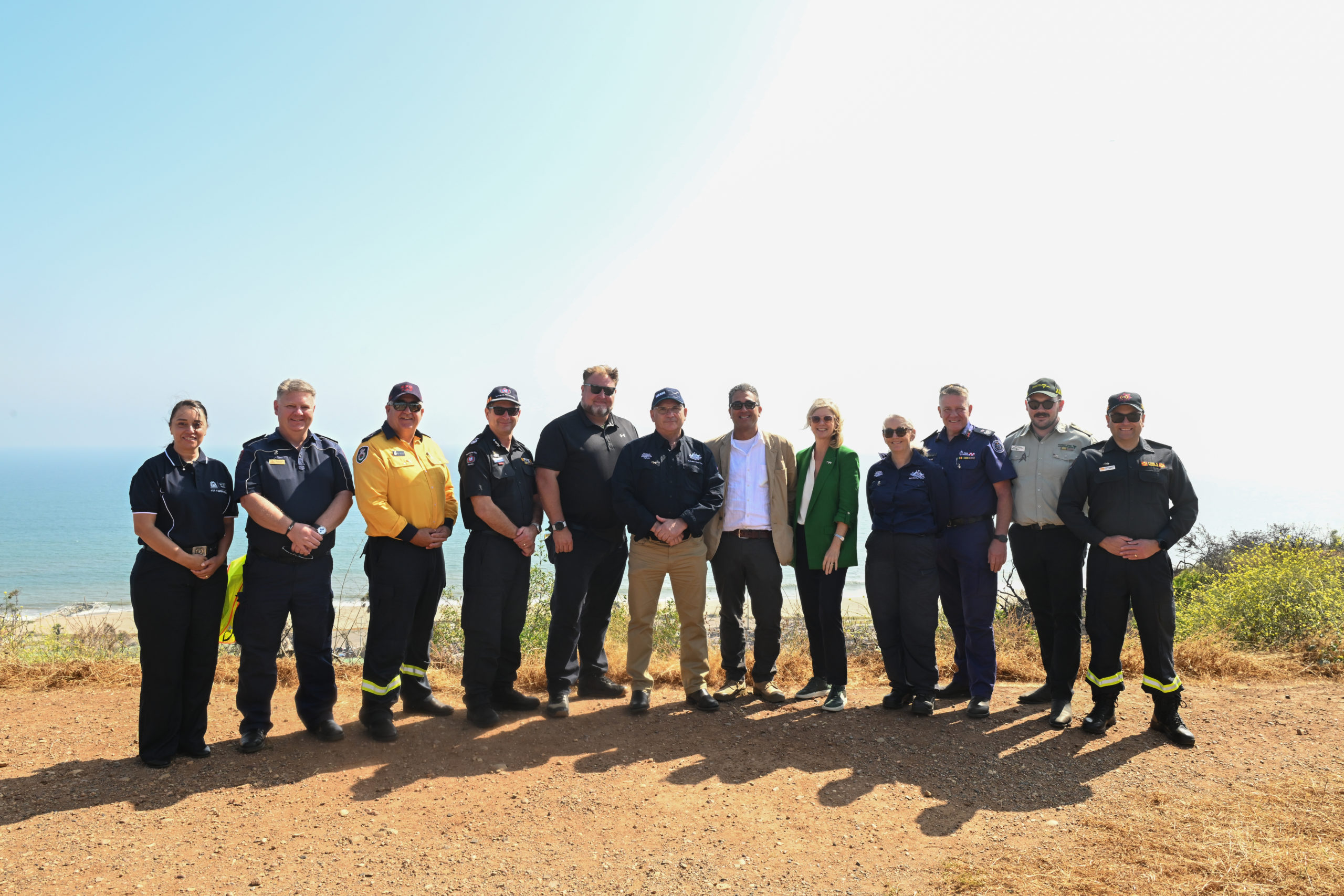 A group of 12 emergency management officials posing for a group photo in front of a view of the ocean